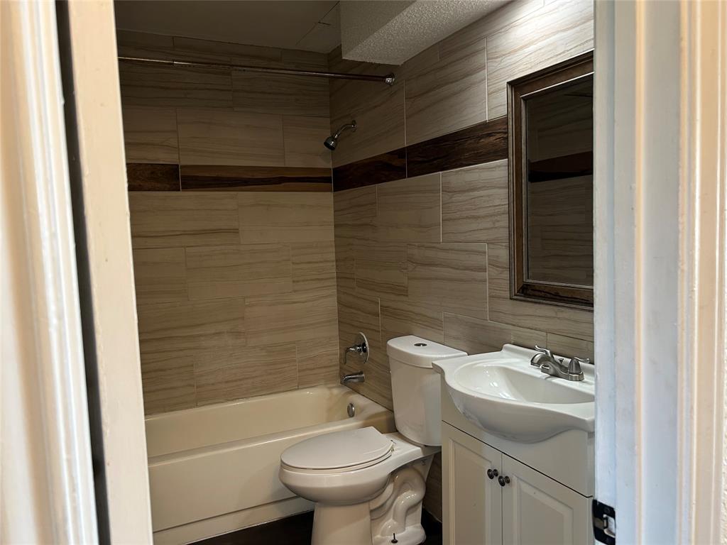 4107 Esters Road Irving, TX 75038 - Photo 9 of 21 Bathroom featuring floor-to-ceiling tile, a full-size bathtub with shower, a modern vanity with a white basin sink, and a framed mirror