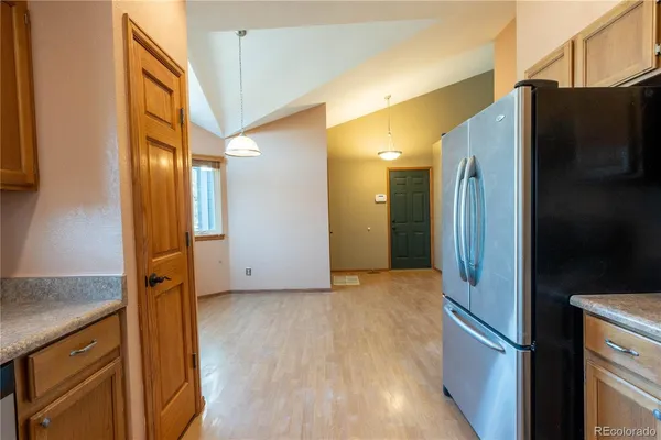 a view of a refrigerator in kitchen and an empty room with wooden floor