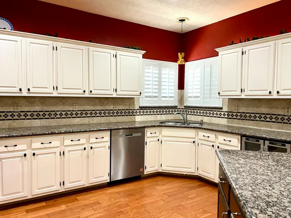 a kitchen with stainless steel appliances granite countertop a stove a sink and white cabinets with wooden floor
