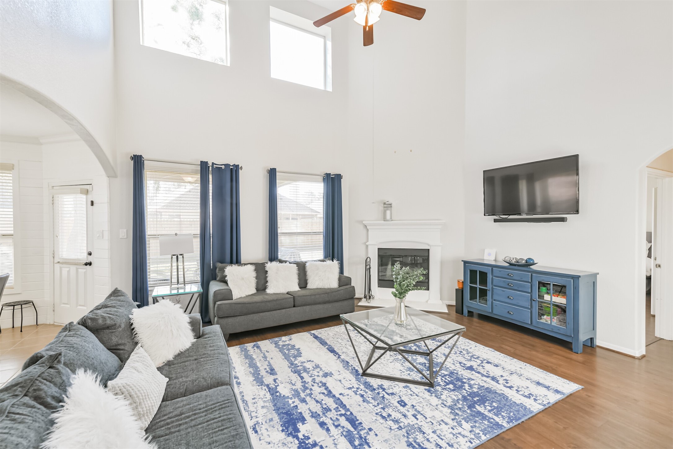 2602 Fort Settlement Trail Spring, TX 77373 - Photo 15 of 50 Spacious two-story family room featuring a ceiling fan and elegant light fixture. Large windows flood the space with natural light, creating a bright and inviting atmosphere. The home boasts extensive laminate wood flooring throughout, adding a seamless and stylish touch.