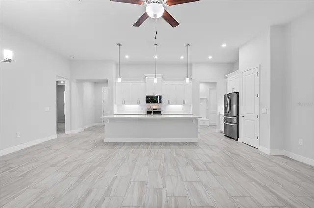 a large white kitchen with a white kitchen island a sink dishwasher and a refrigerator with wooden floor