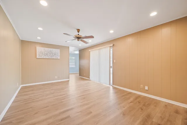 a view of an empty room with wooden floor and a ceiling fan