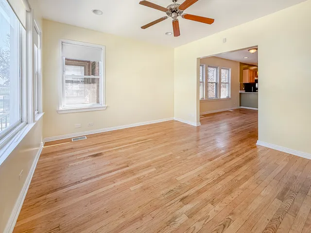 an empty room with wooden floor fan and windows