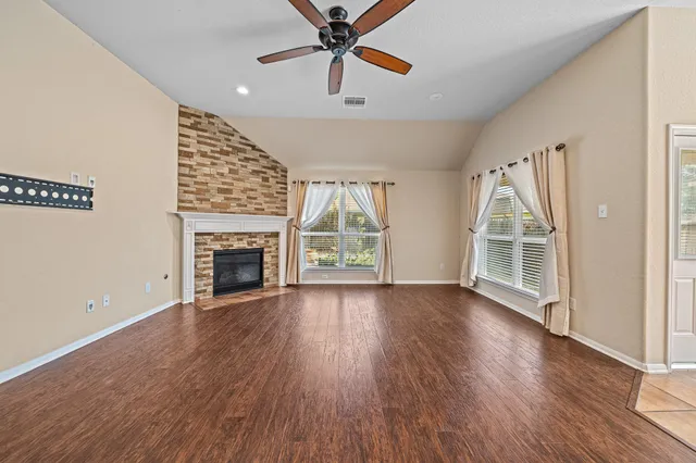 an empty room with windows a fireplace a ceiling fan and wooden floor