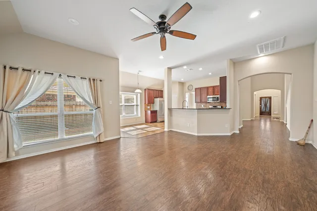 an empty room with wooden floor a ceiling fan and kitchen view