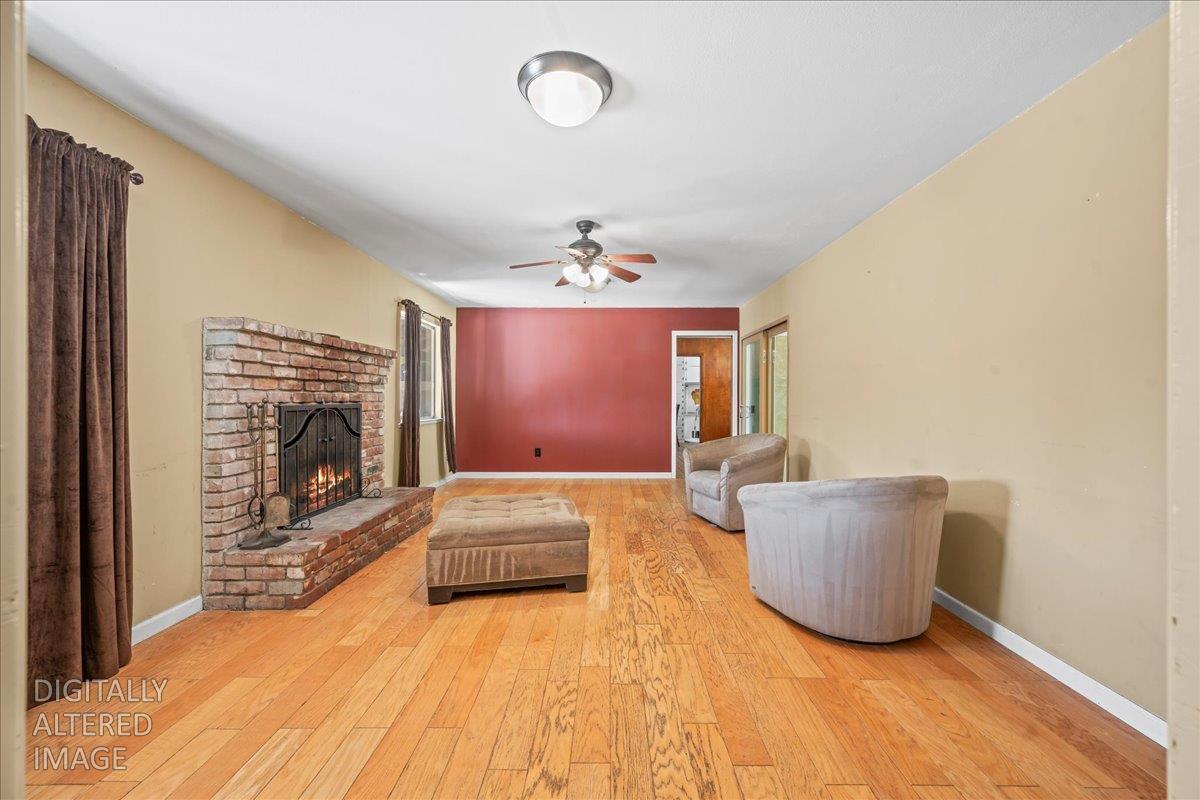 6929 Lisa Marie Way Carmichael, CA 95608 - Photo 4 of 50 Spacious living area featuring wood-finish flooring, a brick fireplace with a raised hearth, and a ceiling fan with integrated lighting. Actual fire was added digitally.