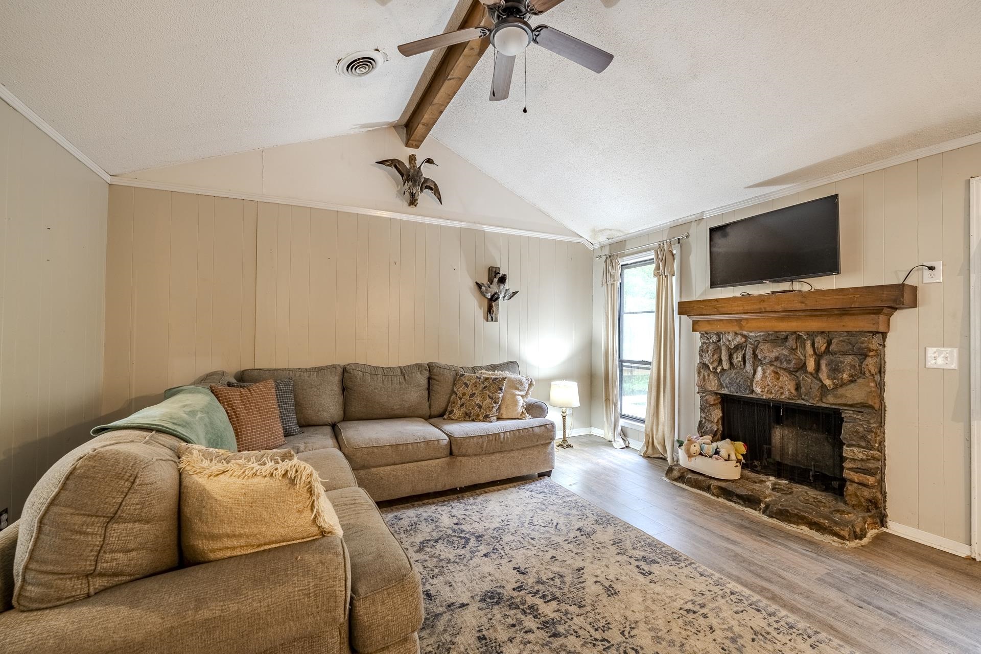 259 Oakview Drive Adamsville, TN 38310 - Photo 6 of 32 Living area featuring a stone-clad fireplace with a wood mantel, vaulted ceiling with exposed wood beam, and a ceiling fan