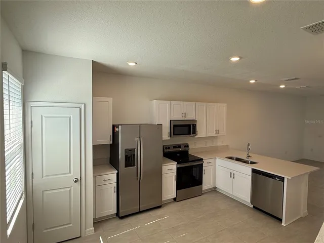 a kitchen with stainless steel appliances a sink a stove a microwave a refrigerator a sink and cabinets