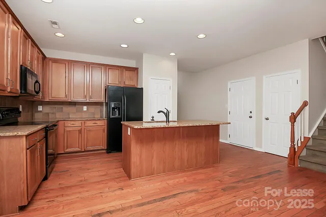 a kitchen with stainless steel appliances granite countertop a refrigerator a sink dishwasher a stove and white countertops with wooden floor