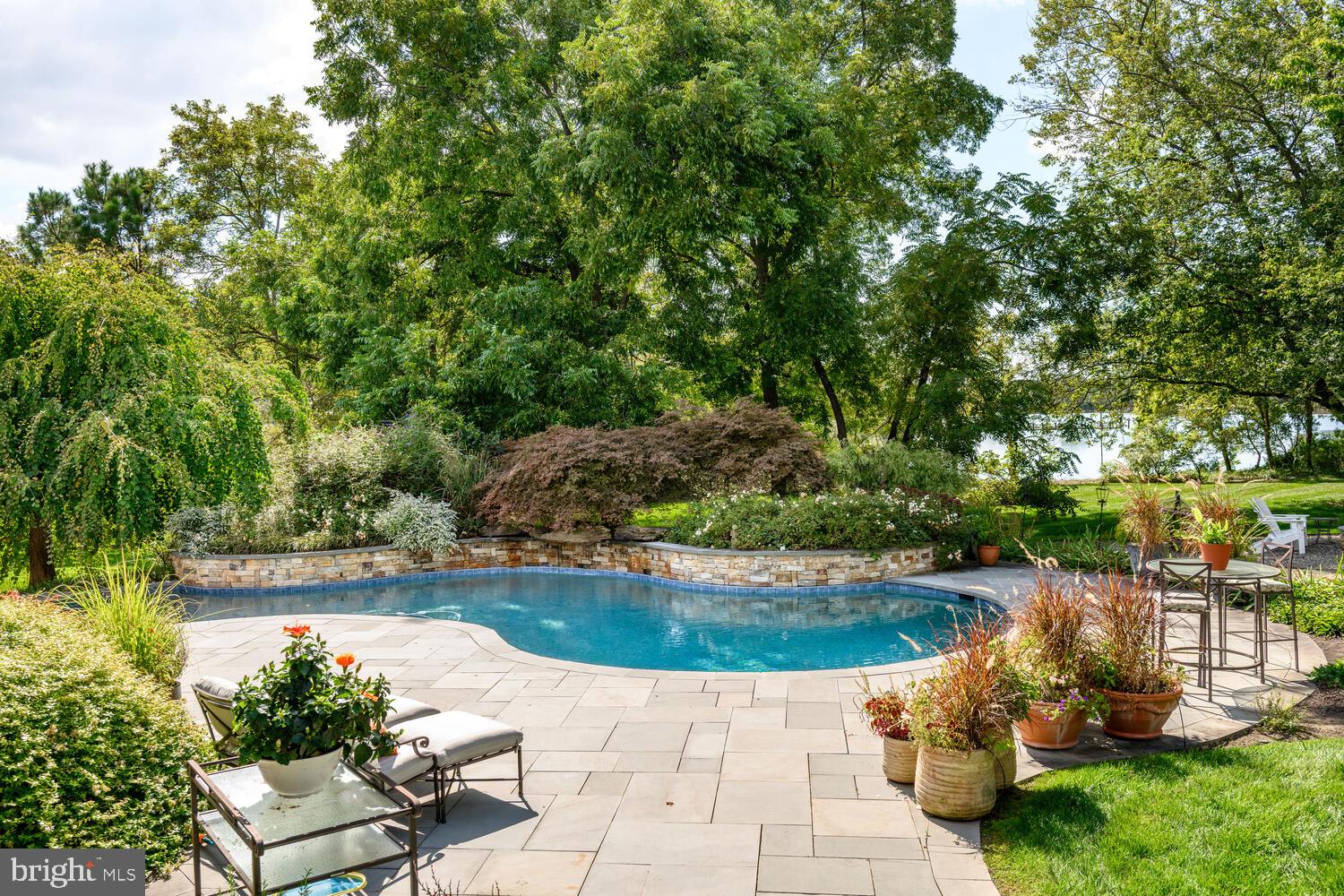 7508 Cooper Point Road Bozman, MD 21612 - Photo 28 of 116 a view of a swimming pool with lawn chairs potted plants and large tree