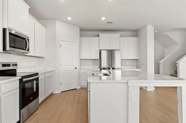 a view of kitchen with granite countertop refrigerator oven sink and white cabinets with wooden floor