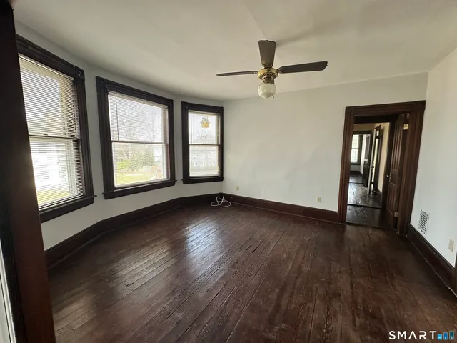 an empty room with wooden floor fan and windows