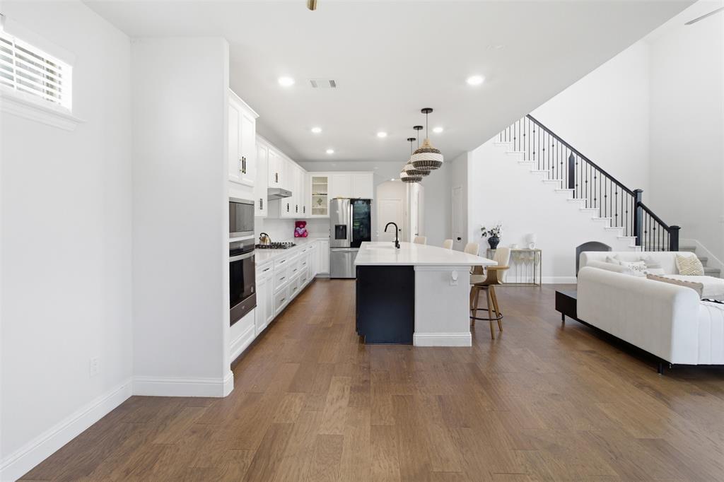 7416 Sequoia Rdg Road Little Elm, TX 76227 - Photo 8 of 37 Open-concept living area featuring wood-finish flooring, a contemporary kitchen with a large island and integrated appliances, and a two-story ceiling with a modern staircase