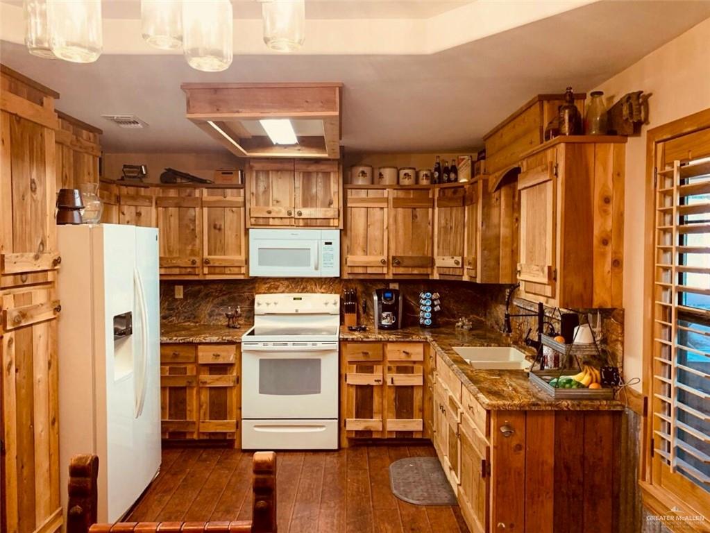 2938 Highway 83 Roma, TX 78584 - Photo 7 of 23 Kitchen with white appliances, dark wood-type flooring, brown cabinets, dark stone counters, and backsplash