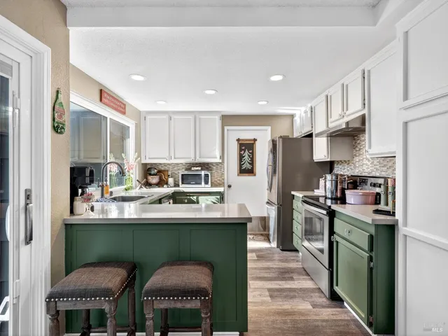 a kitchen with kitchen island stainless steel appliances a sink a stove a refrigerator cabinets and a dining table