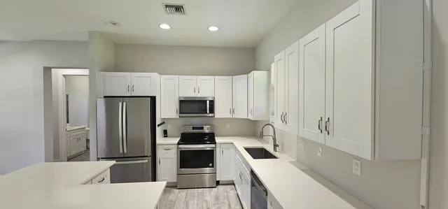 a kitchen with stainless steel appliances a refrigerator a stove a sink and white cabinets