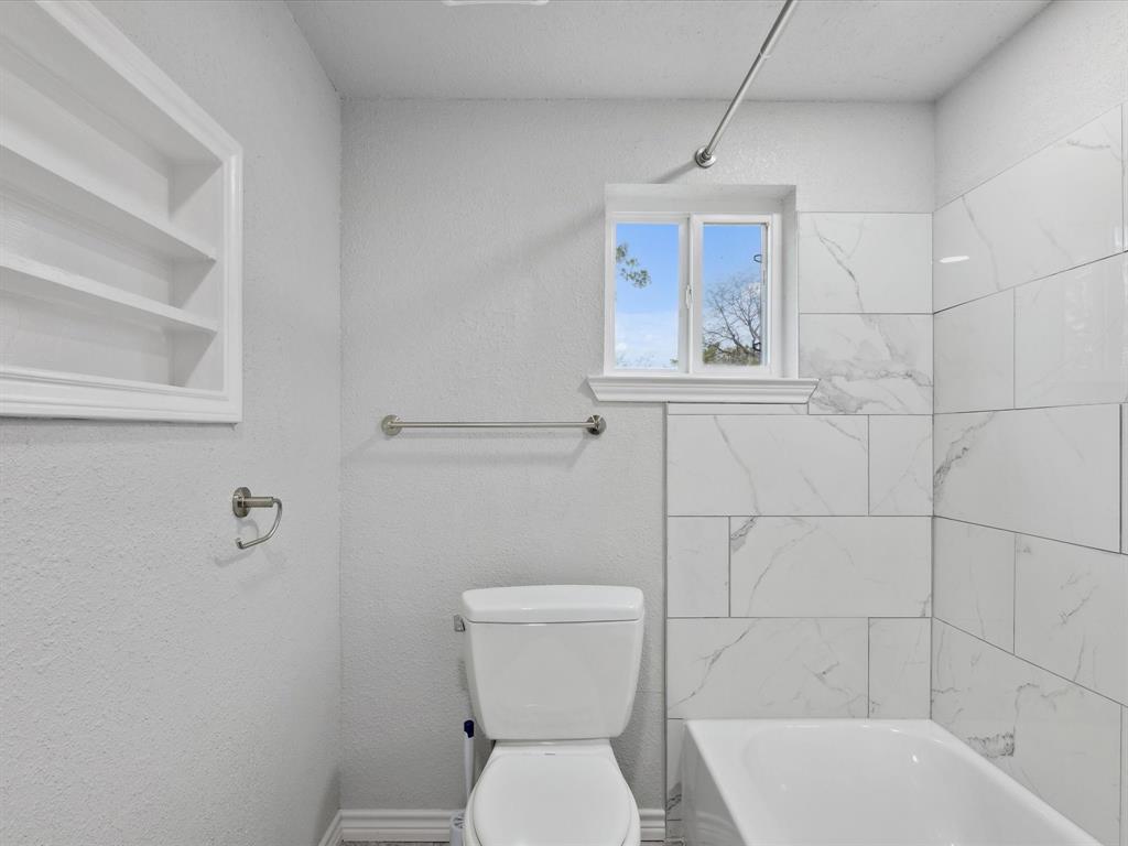 107 East Riley Street Bowie, TX 76230 - Photo 11 of 32 Full bathroom with built in features, toilet, a textured wall, and shower combination