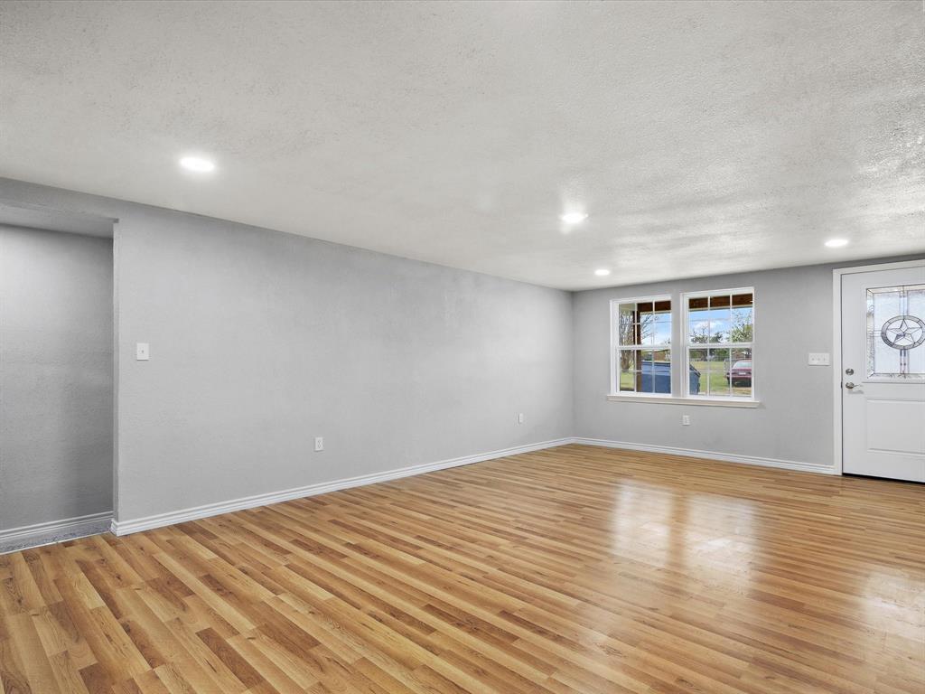 107 East Riley Street Bowie, TX 76230 - Photo 12 of 32 Unfurnished living room with light wood-style flooring, baseboards, and a textured ceiling