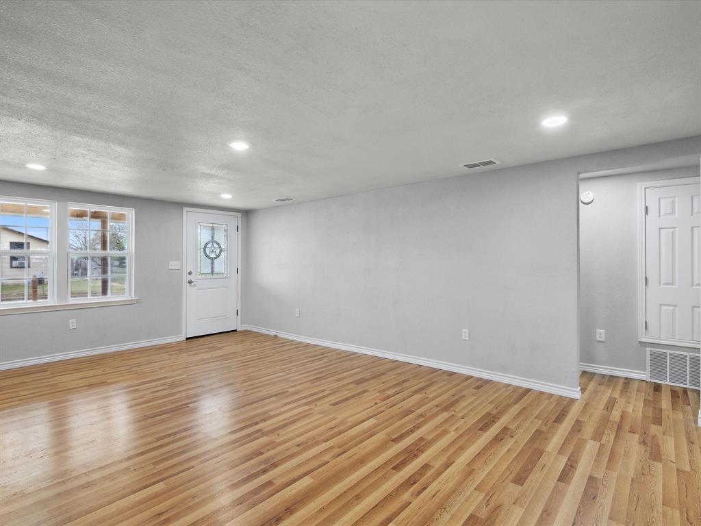 107 East Riley Street Bowie, TX 76230 - Photo 16 of 32 Unfurnished living room featuring light wood finished floors, baseboards, and visible vents