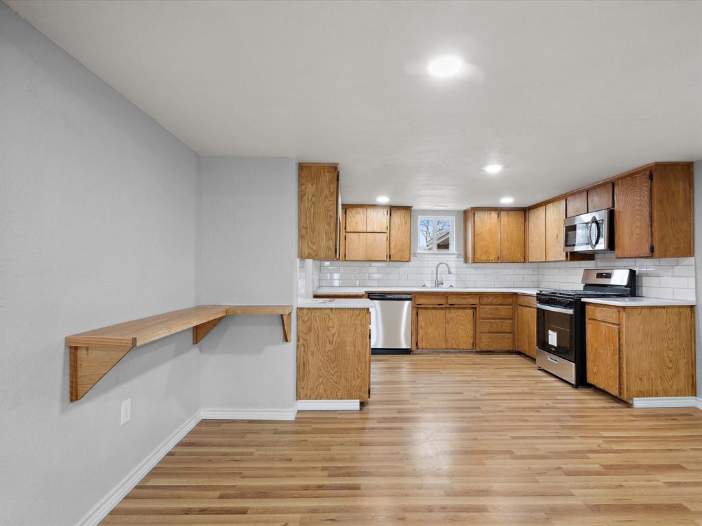 107 East Riley Street Bowie, TX 76230 - Photo 18 of 32 Kitchen featuring backsplash, light countertops, stainless steel appliances, and light wood finished floors