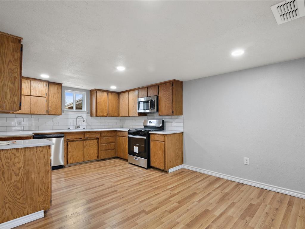 107 East Riley Street Bowie, TX 76230 - Photo 19 of 32 Kitchen featuring light countertops, appliances with stainless steel finishes, brown cabinets, and visible vents