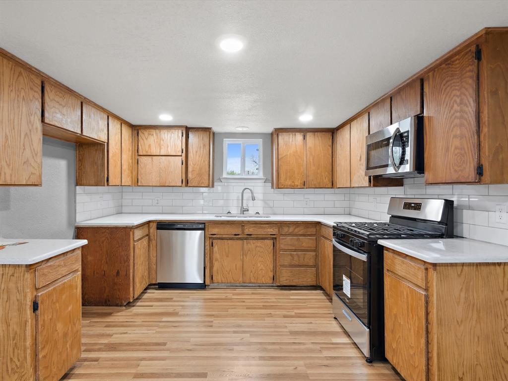 107 East Riley Street Bowie, TX 76230 - Photo 20 of 32 Kitchen featuring a sink, brown cabinetry, light wood-style flooring, and appliances with stainless steel finishes