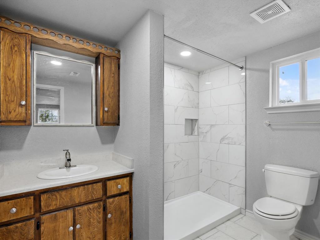 107 East Riley Street Bowie, TX 76230 - Photo 23 of 32 Full bath featuring marble finish floor, toilet, tiled shower, and visible vents