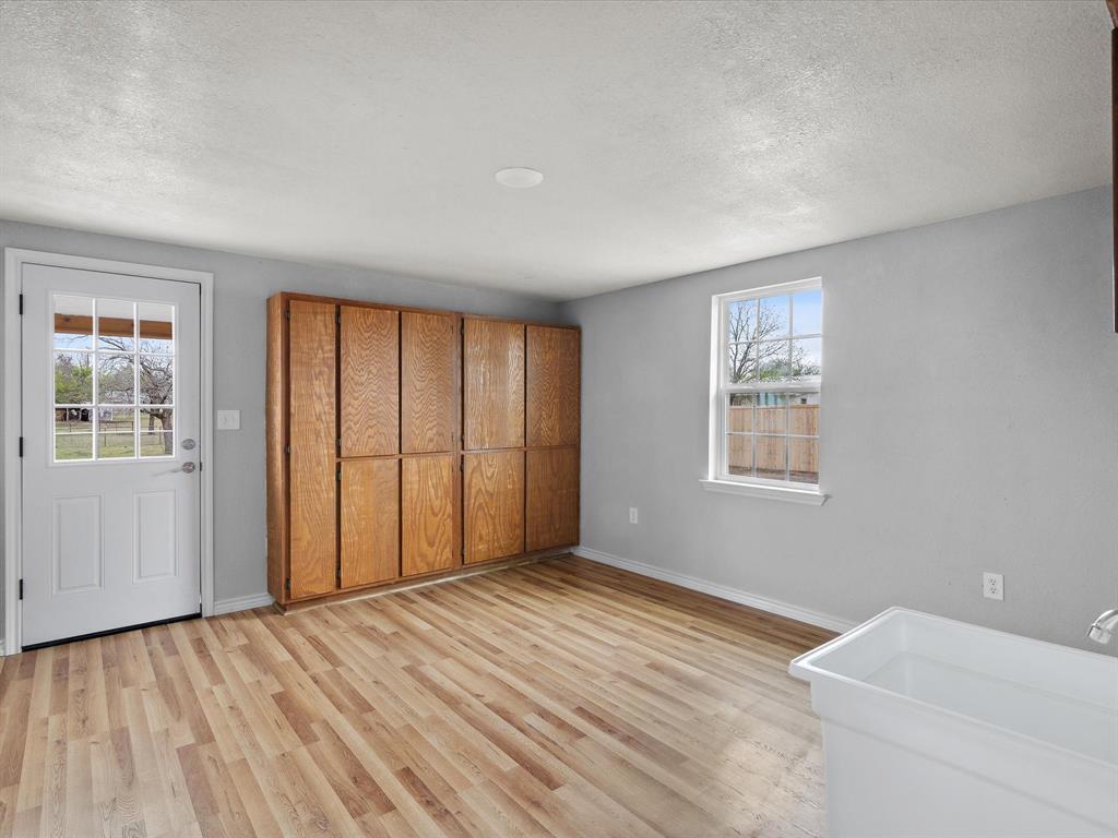 107 East Riley Street Bowie, TX 76230 - Photo 26 of 32 Unfurnished bedroom with multiple windows, light wood-style floors, baseboards, and a textured ceiling
