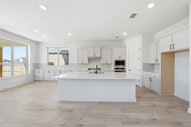 a large white kitchen with kitchen island a stove a sink a refrigerator and white cabinets with wooden floor