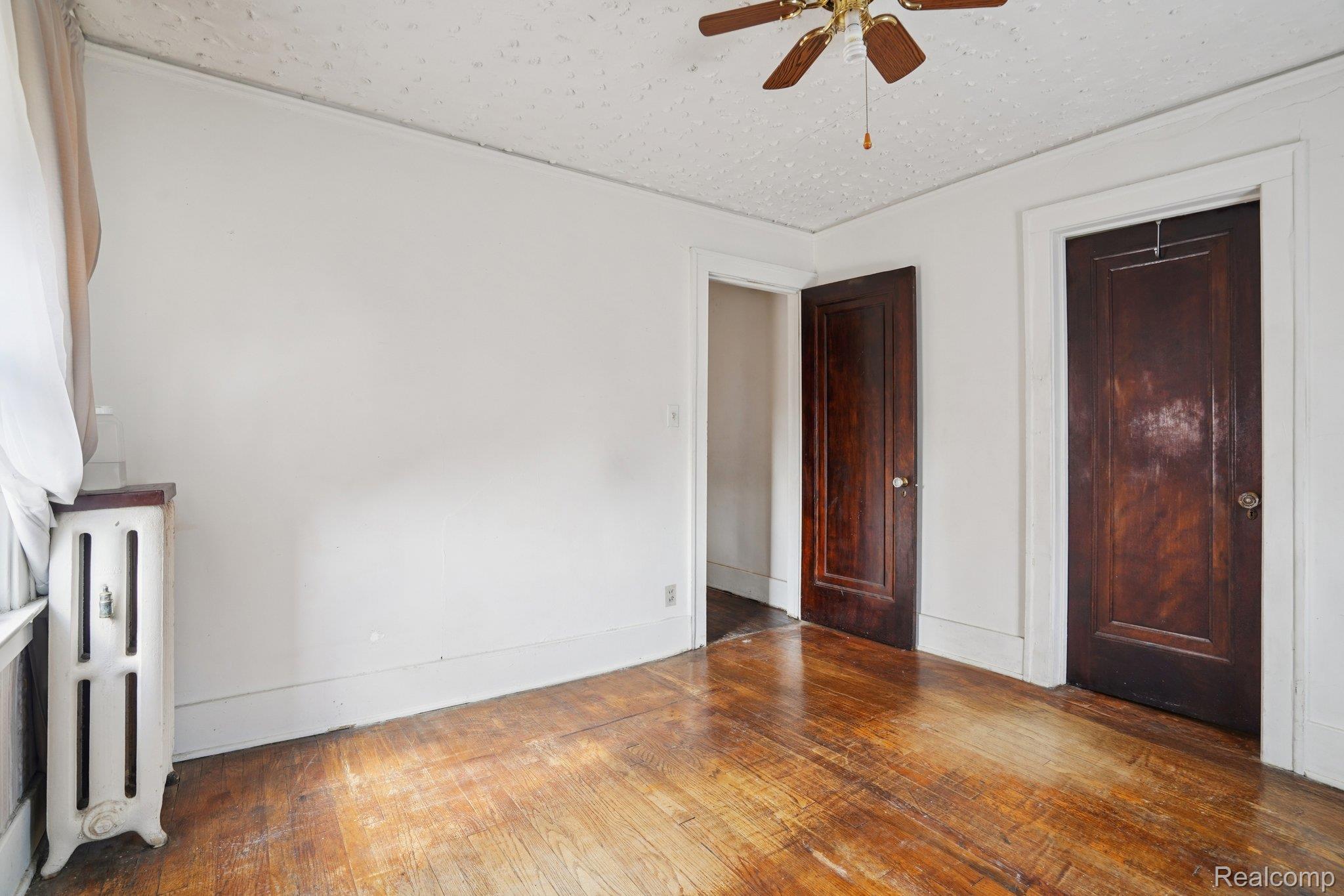 4101 Pasadena Street Detroit, MI 48238 - Photo 37 of 42 Hardwood flooring, two dark wood-finish interior doors, white baseboards, ceiling fan with light fixture, and a cast iron radiator
