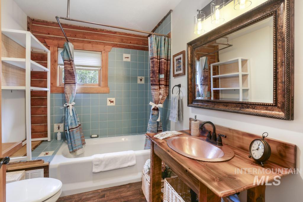 65 Goat Creek Way Stanley, ID 83278 - Photo 26 of 32 Bathroom featuring a copper vessel sink set into a wood-finish vanity, a framed mirror, and a full bathtub with blue tile surround