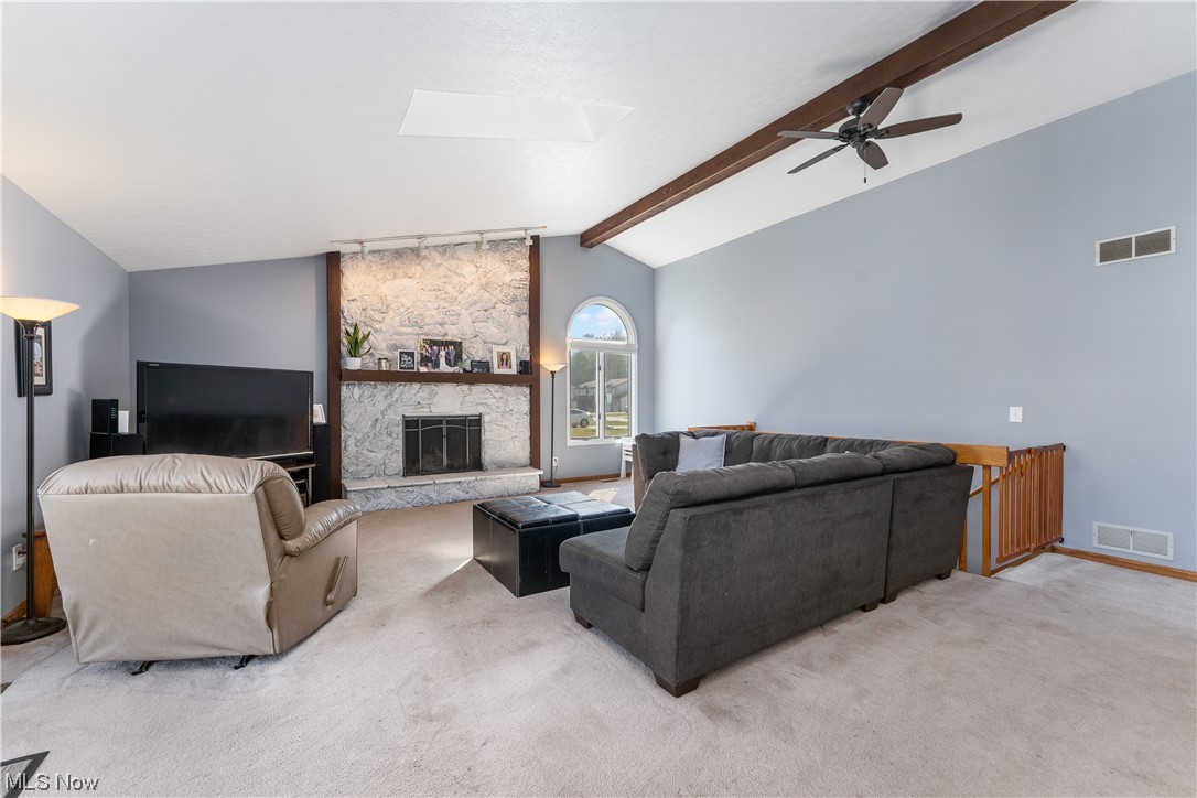 5226 Johnnycake Ridge Northeast Canton, OH 44705 - Photo 12 of 32 Carpeted living room with lofted ceiling with skylight, ceiling fan, and a stone fireplace