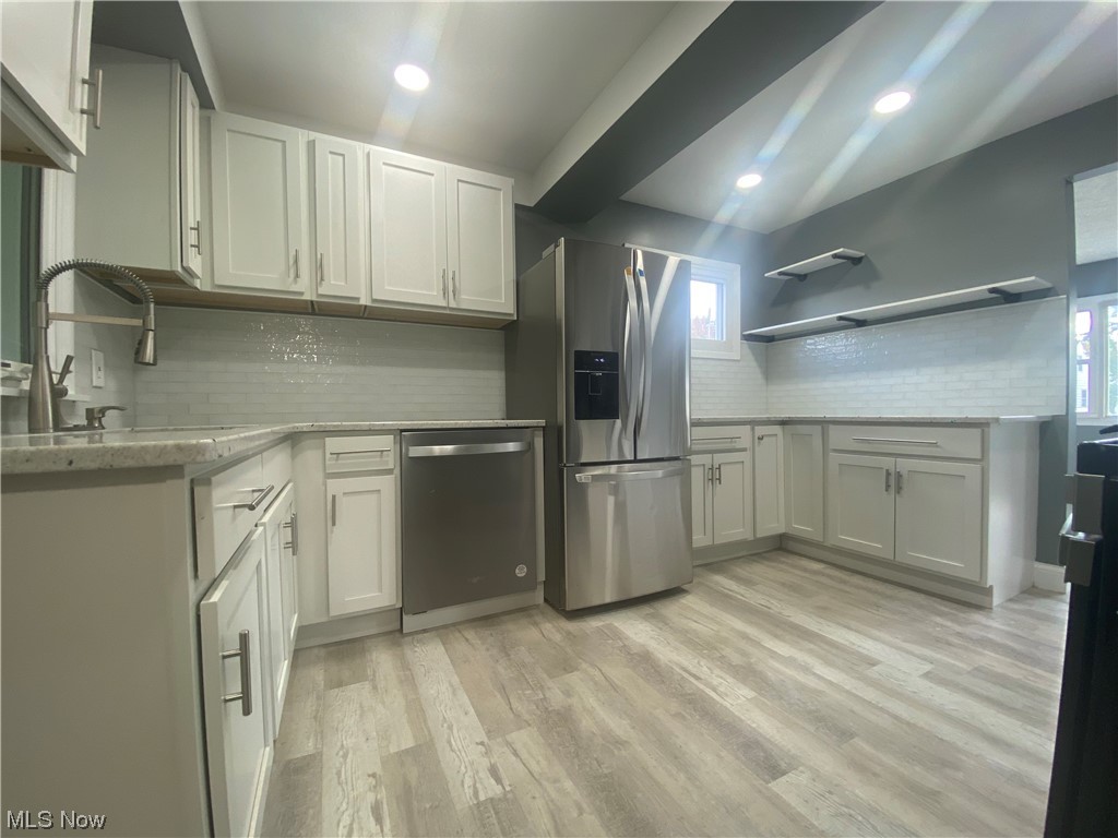 12913 Silver Road Cleveland, OH 44125 - Photo 5 of 23 Kitchen with a wealth of natural light, backsplash, white cabinets, light countertops, light hardwood floors, and stainless steel appliances