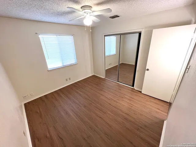 an empty room with wooden floor fan and windows