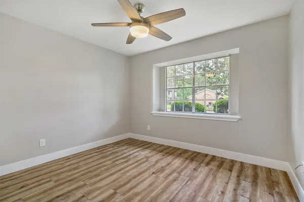a view of an empty room with wooden floor and a ceiling fan