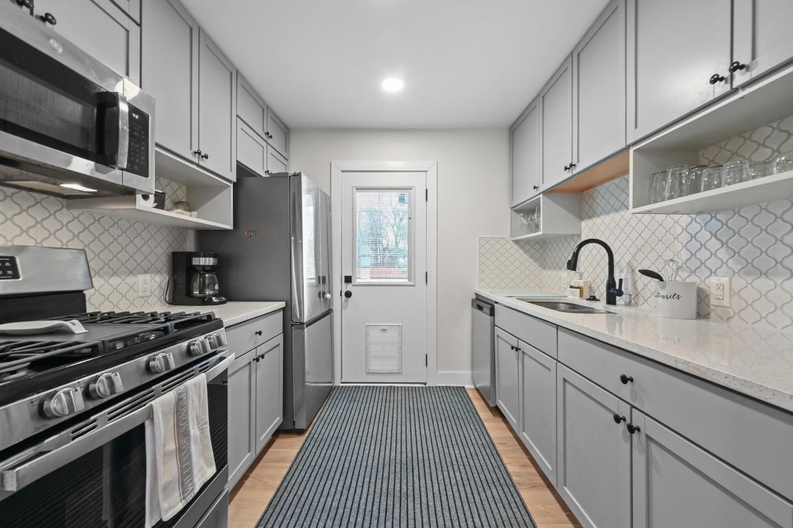 1307 Falcon Cove, Unit A Austin, TX 78745 - Photo 11 of 21 Kitchen with open shelves, gray cabinetry, appliances with stainless steel finishes, light wood finished floors, and recessed lighting