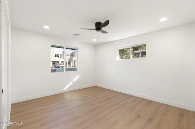an empty room with wooden floor ceiling fan and windows