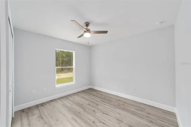 an empty room with wooden floor ceiling fan and windows