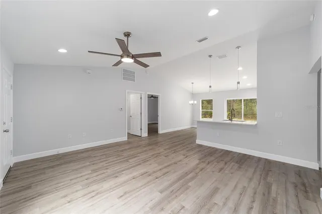 an empty room with wooden floor ceiling fan and windows