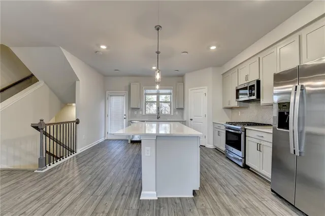 a kitchen with stainless steel appliances kitchen island granite countertop a stove top oven a sink dishwasher a refrigerator and white cabinets with wooden floor