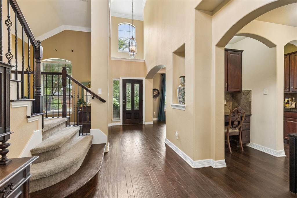 960 Remuda Road Frisco, TX 75033 - Photo 4 of 39 Two-story foyer featuring wood-finish flooring, a grand staircase with wrought iron balusters, a double-height arched window, and a built-in study nook with cabinetry