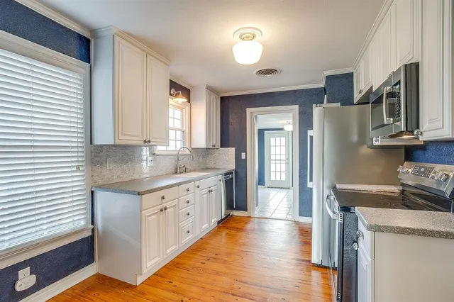 a kitchen with stainless steel appliances granite countertop a refrigerator a sink dishwasher a stove and white countertops with wooden floor