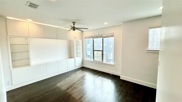 an empty room with wooden floor fan and windows