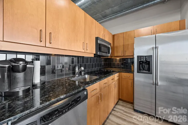 a kitchen with stainless steel appliances granite countertop a refrigerator a stove and a sink with wooden cabinets