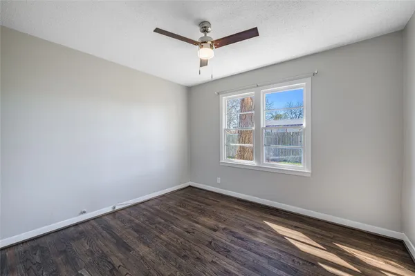 an empty room with wooden floor ceiling fan and windows