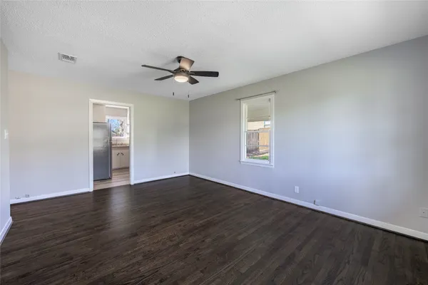 a view of an empty room with wooden floor and a ceiling fan