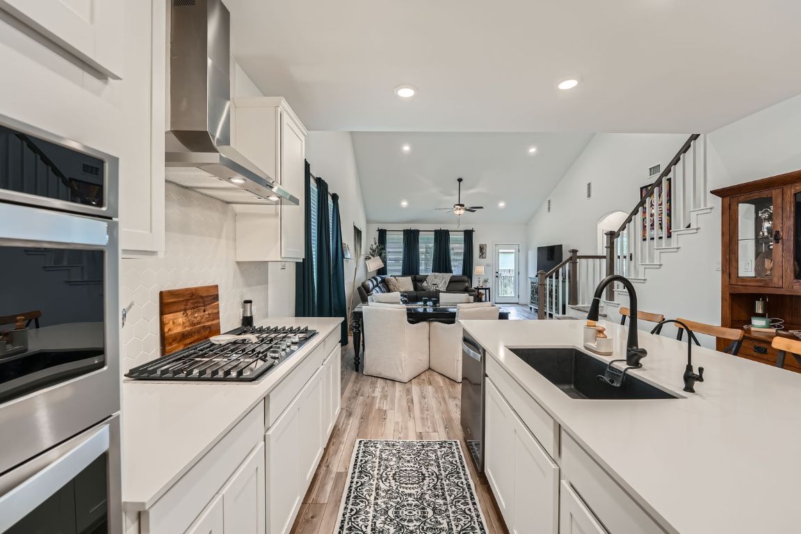 321 Georgia Lace Trail Georgetown, TX 78626 - Photo 28 of 28 Kitchen featuring white cabinetry, open floor plan, light wood finished floors, appliances with stainless steel finishes, and wall chimney exhaust hood