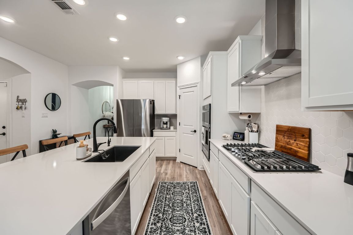 321 Georgia Lace Trail Georgetown, TX 78626 - Photo 10 of 28 Kitchen with white cabinetry, light wood finished floors, wall chimney exhaust hood, appliances with stainless steel finishes, and decorative backsplash
