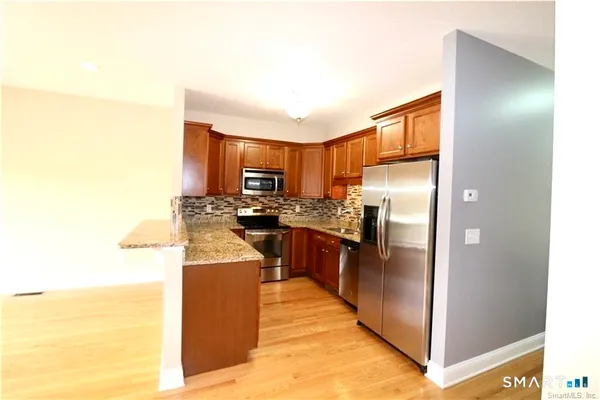 a kitchen with stainless steel appliances granite countertop a refrigerator a stove and a sink with wooden floor