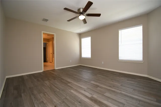an empty room with wooden floor ceiling fan and windows